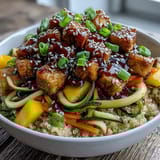 Golden-brown crispy baked tofu cubes and vibrant spiralized zucchini and carrots top a fluffy bowl of Easy Teriyaki Quinoa, garnished with sweet mango.