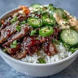 Korean Beef Power Bowl with spicy sriracha mayo drizzle, sesame seeds, and fresh jalapeños atop fluffy rice.