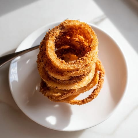 Crispy battered onion rings stacked high, showcasing the tender sweet onion inside, ready to be dipped in creamy ranch dressing.