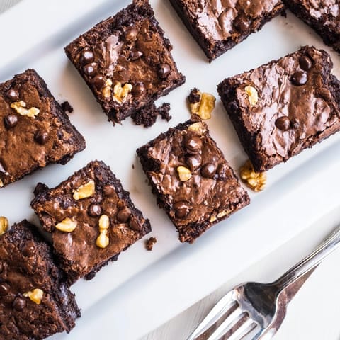 A close-up of a freshly cut brownie reveals its rich cocoa interior, dense texture, and a handful of chopped walnuts inside.