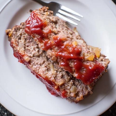 Savory homemade meatloaf with ketchup glaze served alongside mashed potatoes and green beans.