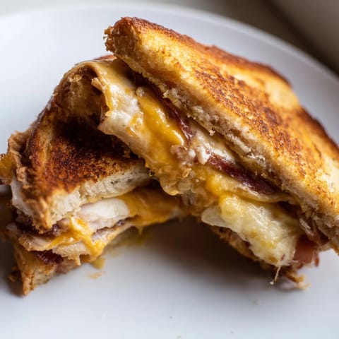 Golden brown sourdough bread is grilled, stuffed with melted cheddar, roasted turkey, bacon, lettuce, and tomato, making a delicious Turkey Club Grilled Cheese.