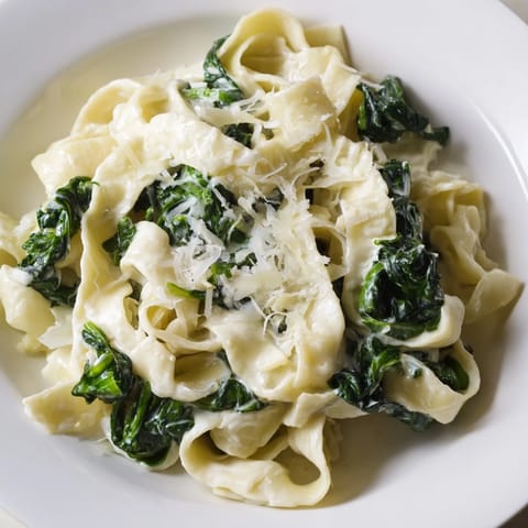 A close-up of tender egg noodles coated in velvety cream sauce, topped with grated Parmesan and wilted spinach.