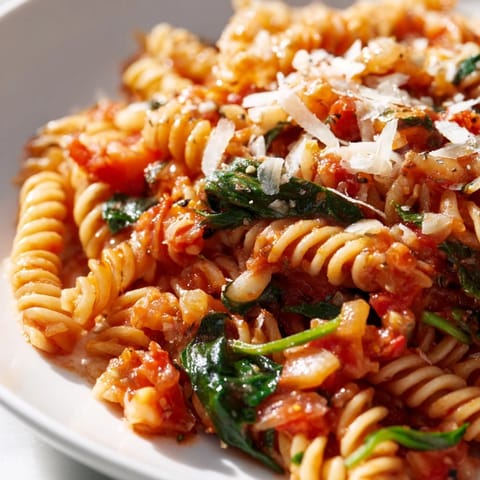 Hearty Tomato Spinach One-Pot Rotini served in a white bowl, garnished with fresh basil and melted Parmesan.  
