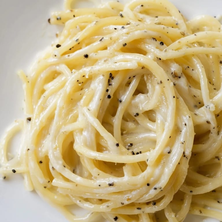 Close-up of Spaghetti Cacio e Pepe garnished with extra grated Pecorino and cracked pepper, served warm on a rustic plate.