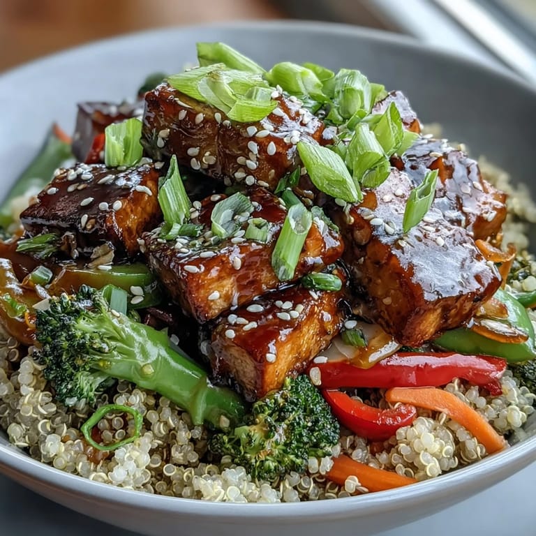 A close-up view of a wholesome Quinoa Vegetable Teriyaki Bowl, featuring golden tofu, broccoli, bell peppers, and a glossy sauce drizzle.