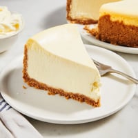 Freshly baked New York Cheesecake with a golden graham cracker crust and creamy vanilla filling, served on a rustic wooden table.