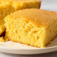 Freshly baked golden cornbread with a crisp edge sits in a square pan, its tender crumb inviting for a cozy meal.