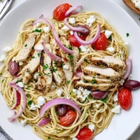 Freshly grilled chicken slices and halved cherry tomatoes tossed with spaghetti in a skillet for Greek Chicken Spaghetti.