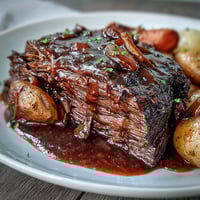 Golden-brown beef pot roast with tender carrots and potatoes in rich red wine gravy on a rustic platter.