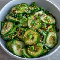 Crisp Asian cucumber salad with sesame and rice vinegar dressing, garnished with sesame seeds and green onions for a refreshing appetizer.
